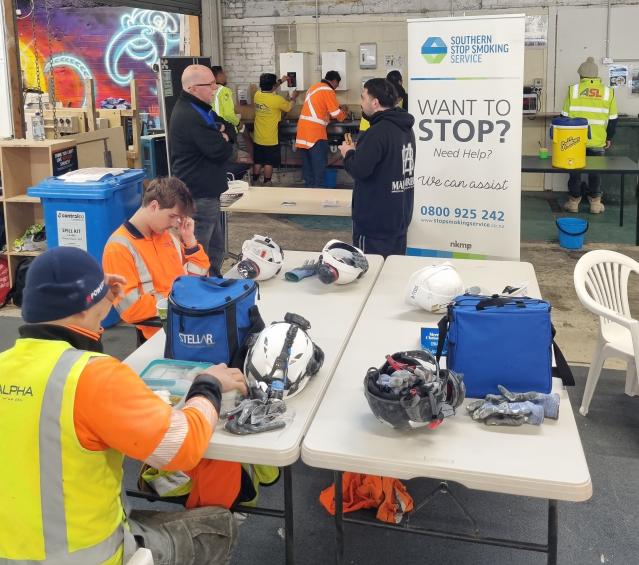 Workers on a building site talking to health promotors and eating lunch.
